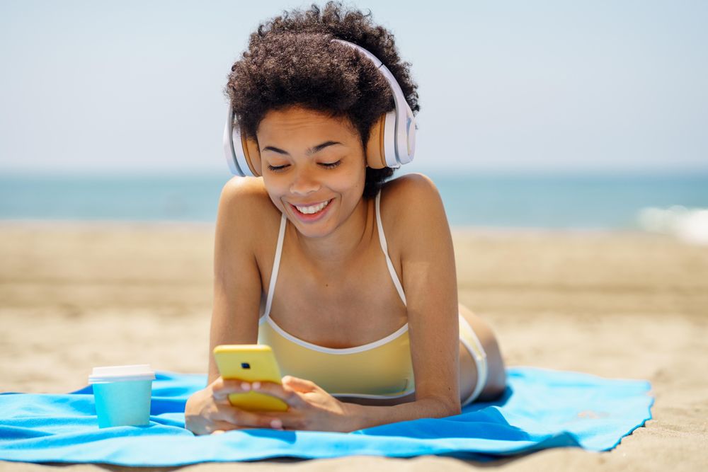 Female with curly hair on beach towel smiling at phone