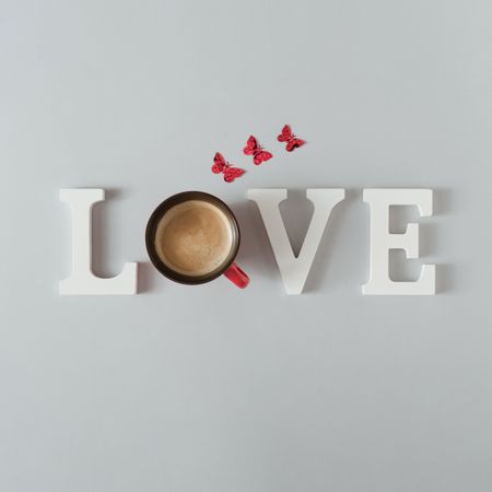 “Love” made of coffee cup with butterflies on grey background