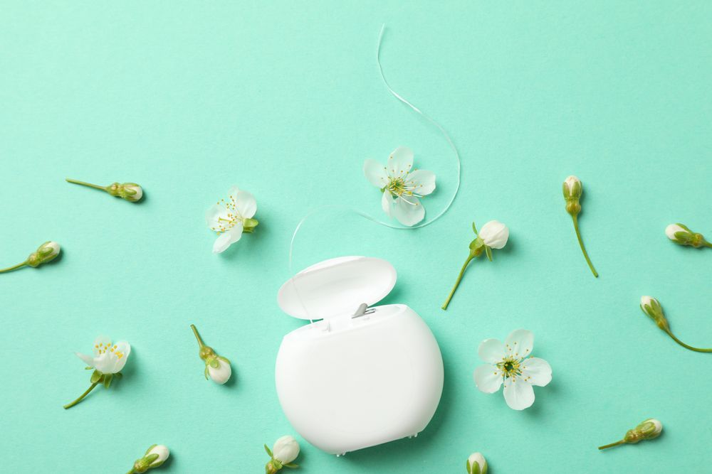 Dental floss and flowers on mint background, top view
