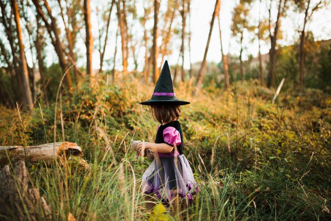 Little girl in witch costume walking through the forest
