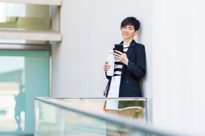 Woman leaning outside building with water bottle