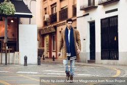 Man in scarf and coat walking through Spanish town 4djkr0