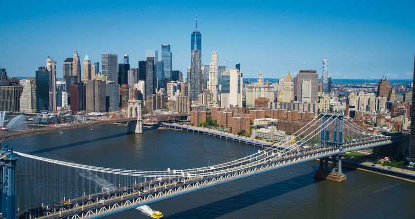Iconic New York City Landscape Over East River with Skyscrapers, Manhattan and Brooklyn Bridges, Cars and Ferry Boats. Cinematic Urban Skyline with Clear Blue Sky