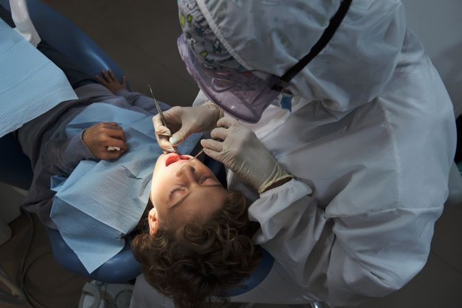 Dentist examining teeth of kid with tools in dental office