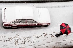 Top of red and dark umbrella shielding person from snowfall walking on street