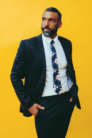 Serious Black male in navy suit with floral tie in yellow studio