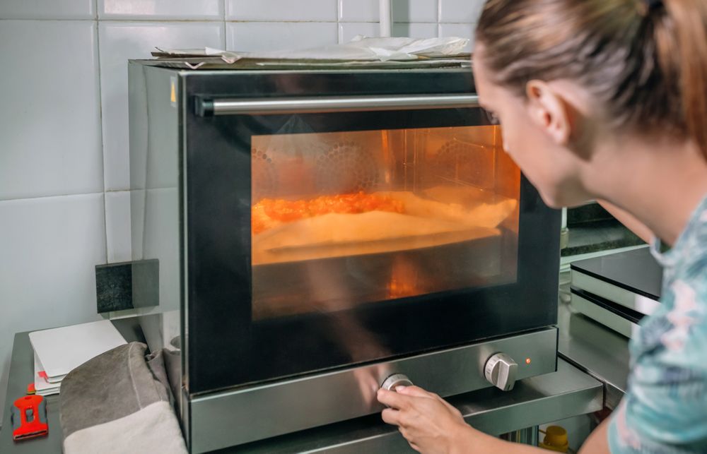 Unrecognizable professional chef adjusting oven temperature while baking pizza in restaurant kitchen
