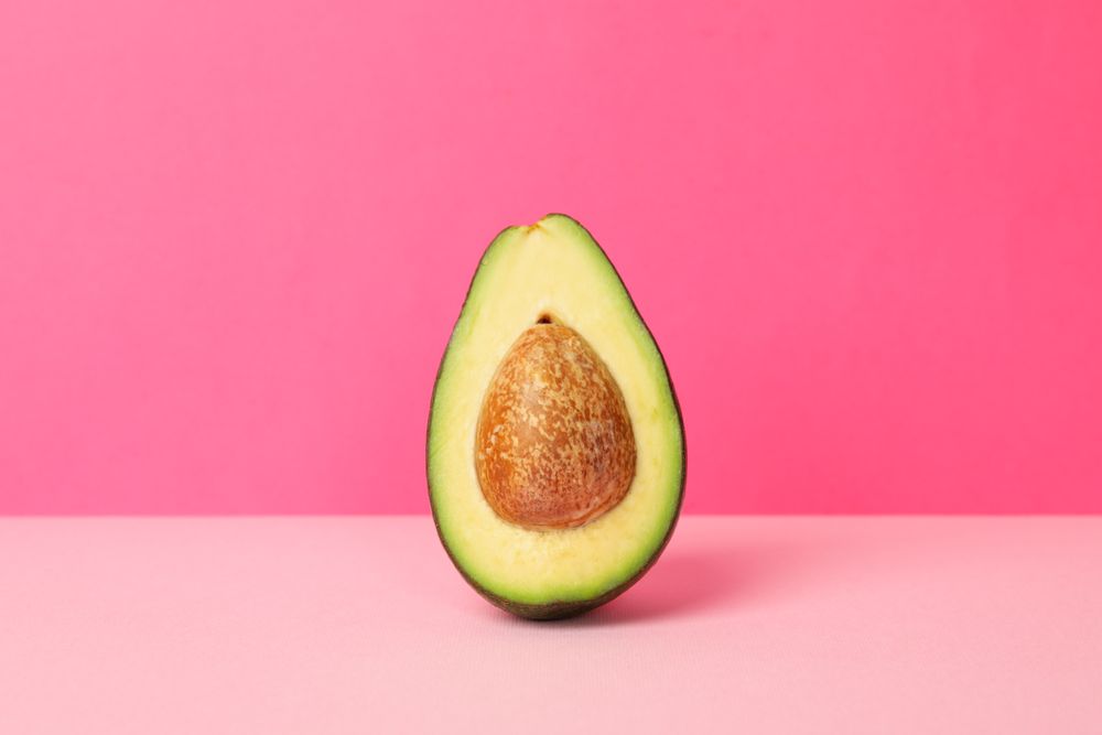 Ripe fresh avocado on pink background, space for text