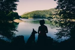 Woman with dog resting against beautiful lake