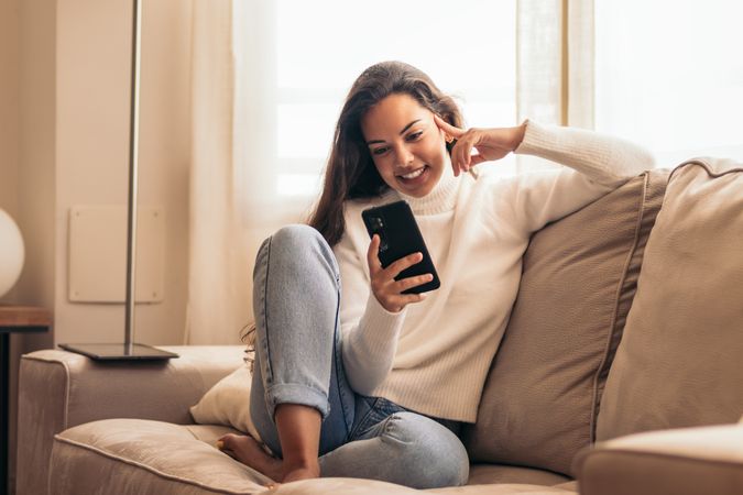 Connected at Home: Young Woman Sitting on Sofa Using Smartphone