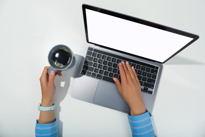 Top view of person using silver laptop with mockup screen on desk and cup of coffee
