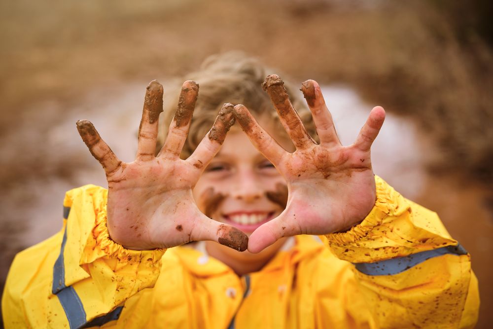 Boy in raincoat looking at camera through fingers while standing