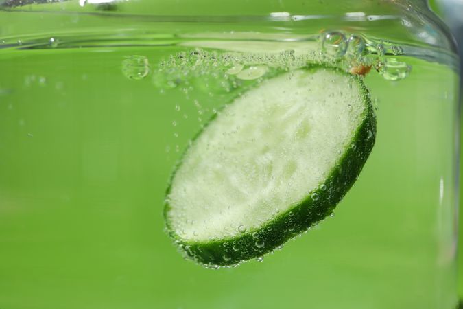 Slice of cucumber submerged in water with copy space