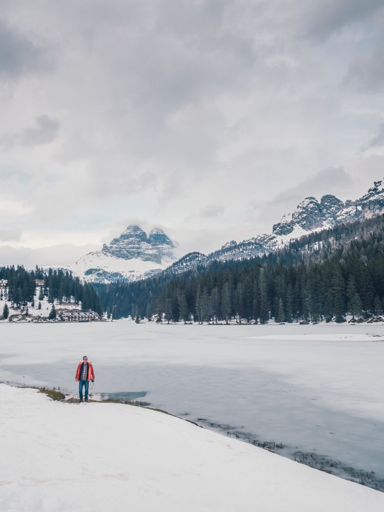 Unrecognizable person standing in snow surrounded by forest and mountains
