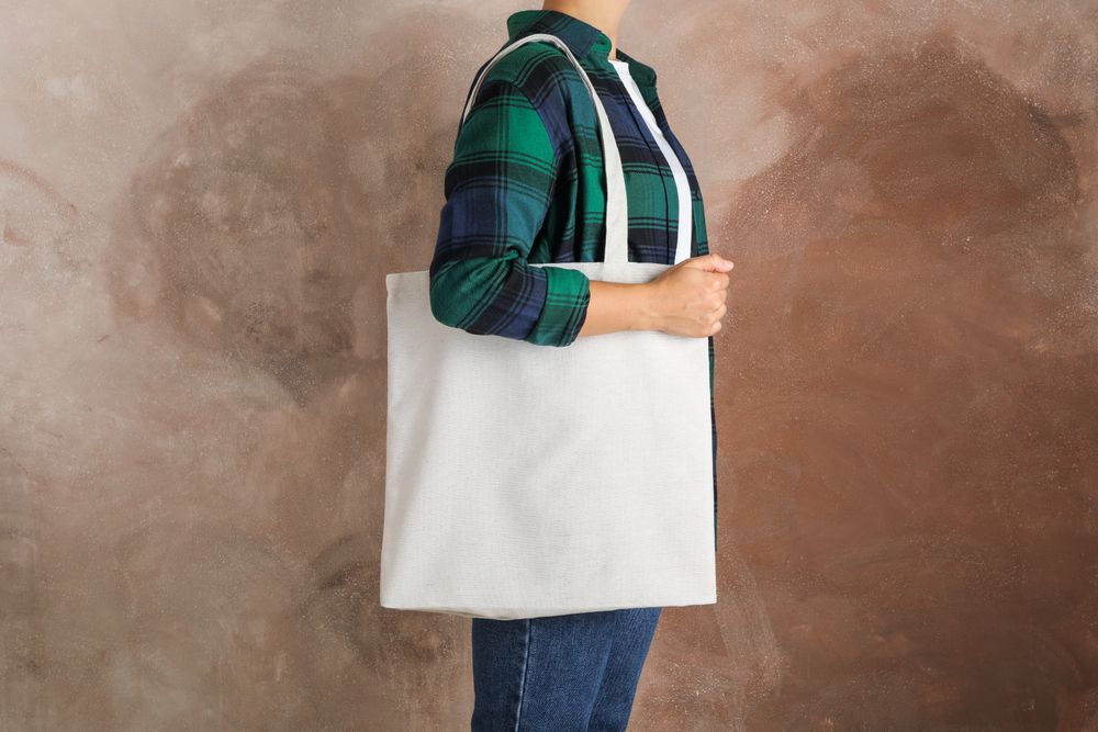 Young woman holding tote bag against brown background, empty space