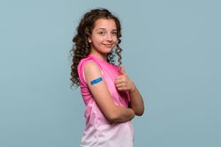 Girl giving thumbs up with blue bandage after vaccination.