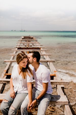 Glad lovers sitting on destroyed pier on seashore