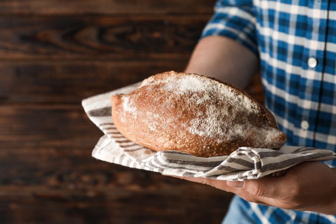 Male hands hold wheat bread against wooden background, space for text Male hands hold wheat bread against wooden background, space for text