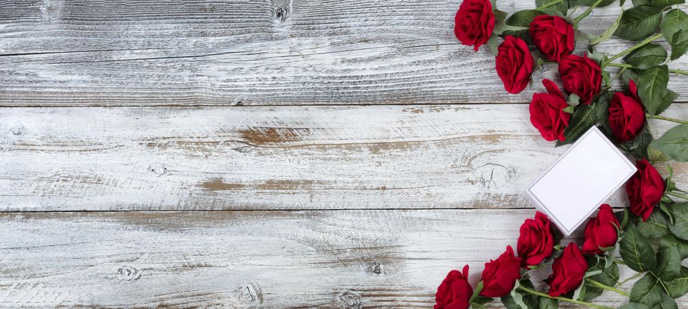 Valentine’s Day small gift box with a dozen red roses on wood