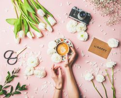 Coffee, tulips on pink background, with “happy” card, and hands on coffee, square crop