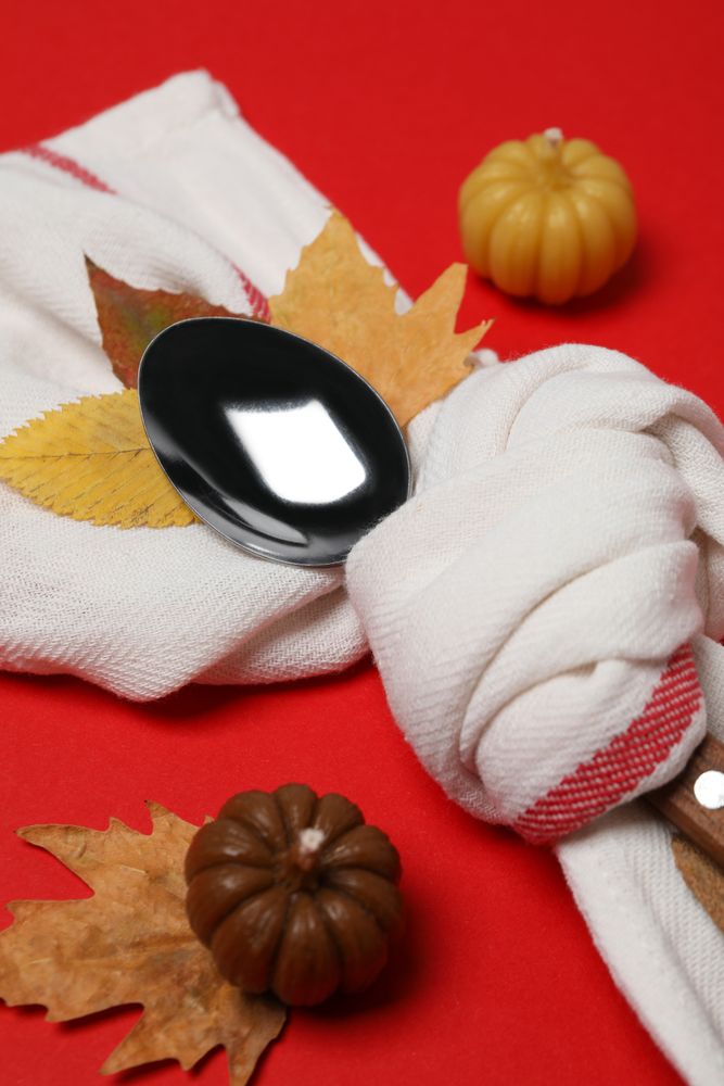 Spoon in towel, leaves and pumpkins on red background