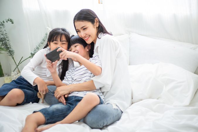 Mother cuddling son and daughter while they play on smartphone