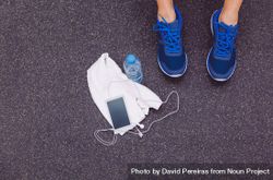 Feet of person wearing blue sneakers on gym floor next to towel, phone and water bottle 0Wory0