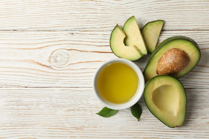 Ripe fresh avocado and oil on wooden background, top view