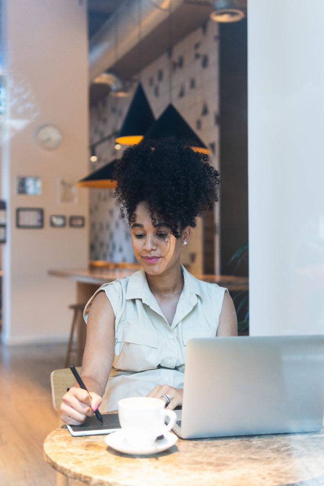 Smiling Black woman working on graphic tablet in cafe