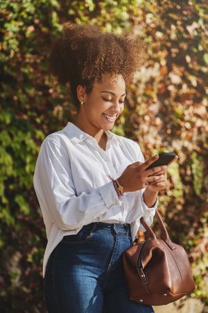 Black woman browsing smartphone near bush on street