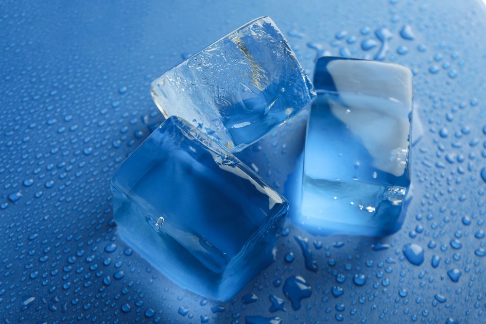 Close up shot looking down at top view of four melting ice cubed on blue table