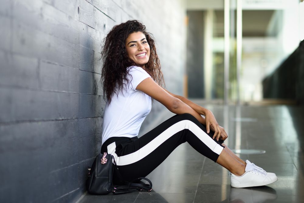 Smiling female in leggings sitting outside of building entrance