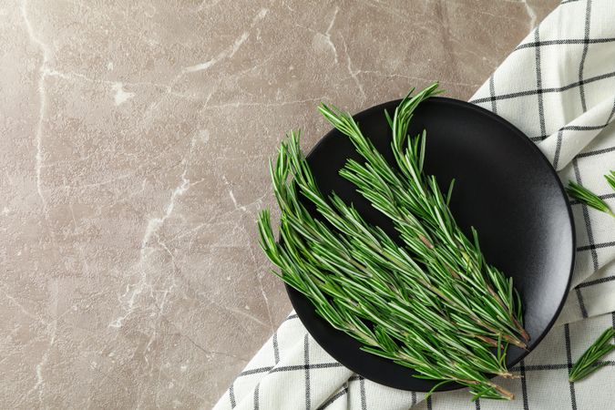 Plate with rosemary and towel on grey table, top view