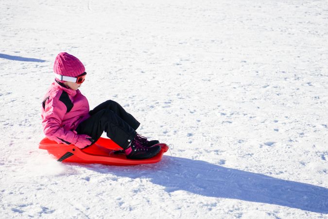 Child in pink snow suit sledding at resort