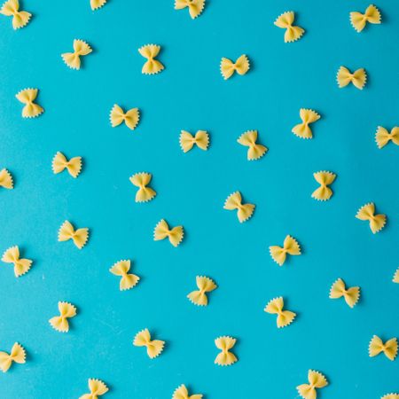 Pattern made of bow-tie pasta on blue background
