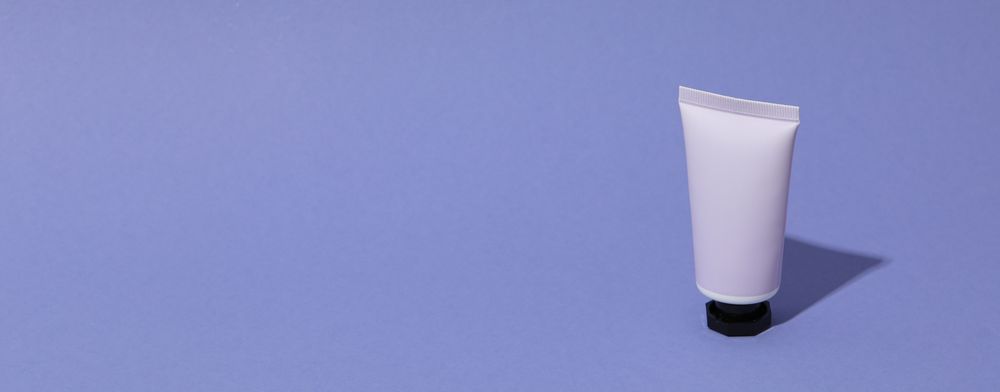 Tube with cream on purple background, space for text