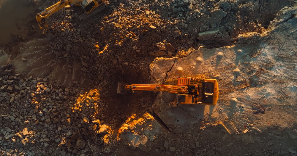 Aerial Drone Shot Directly Above Industrial Excavator Digging Up Rocks On Construction Site On Sunny Day. Workers Operating Machinery To Complete Real Estate Project Or Extract Natural Resources