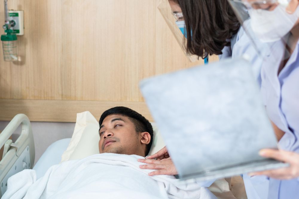Patient with eyes closed in emergency room with doctor & nurse treating him