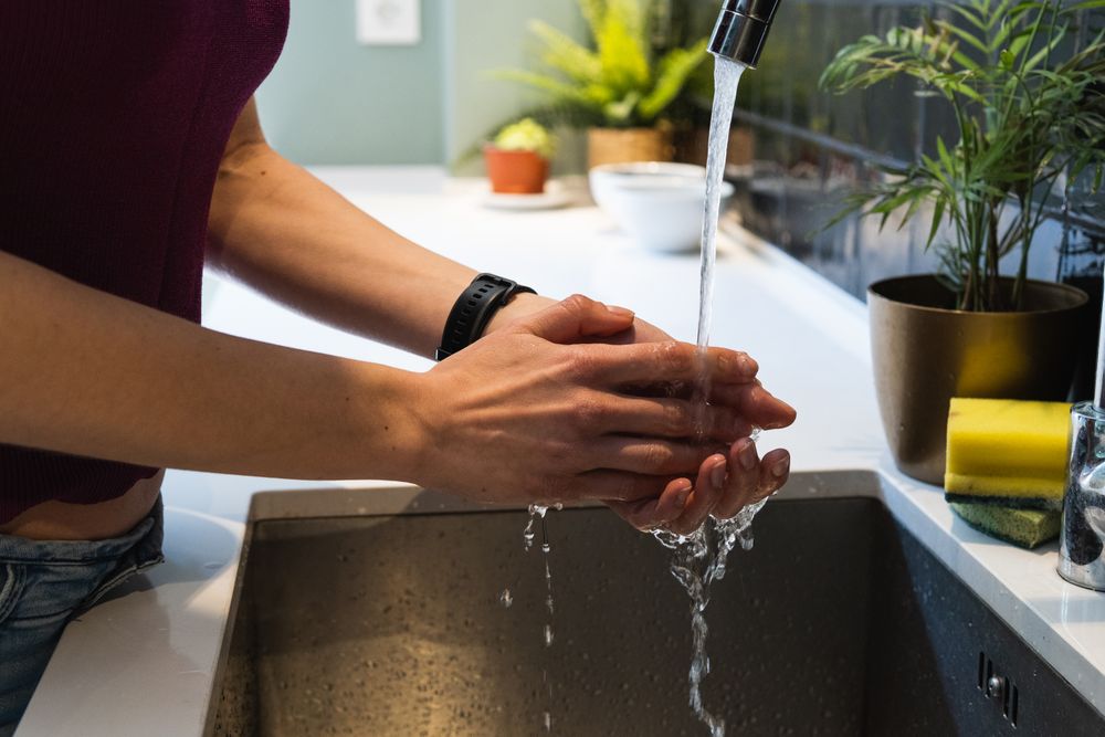 Crop woman washing hands above sink at home