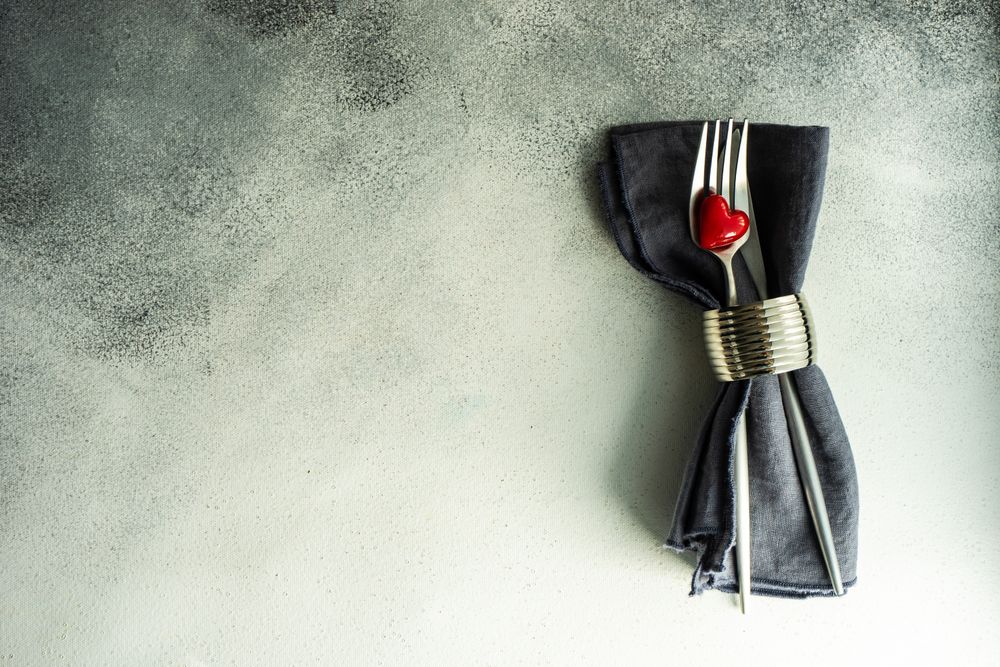 St. Valentine day card with napkin, silverware and heart decorations on grey counter with space for text