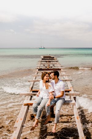 Glad lovers sitting on destroyed pier on seashore