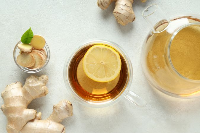 Cup and teapot with tea, ginger on light background, top view