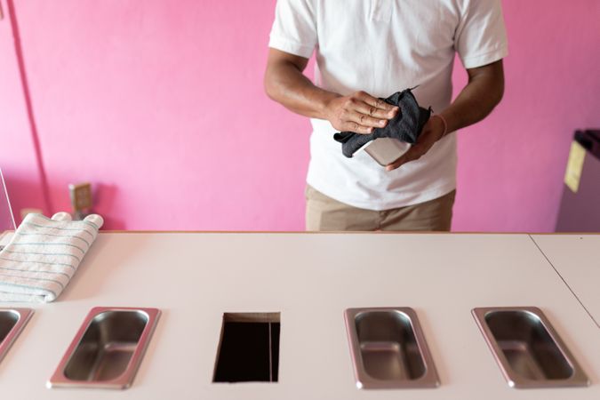 An ice-cream parlor worker is cleaning a metal flavor tray with a cleaning cloth before opening