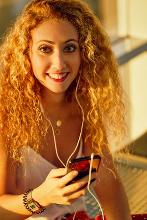 Smiling woman sitting on metal bench with earphones and smartphone