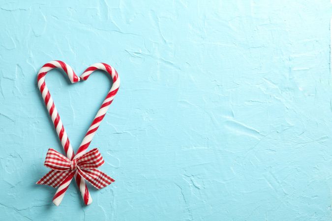 Sweet candy canes with bows on blue background, space for text