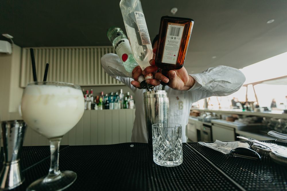 Barman pouring cocktail and alcoholic drinks to shaker in a bar.