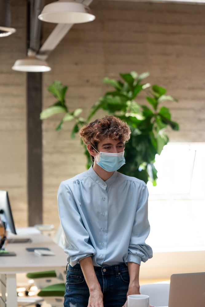 Nonbinary person standing in a bright modern office wearing a face mask