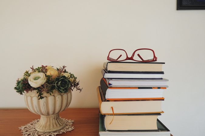 Flower vase beside stack of books with eyeglasses on top