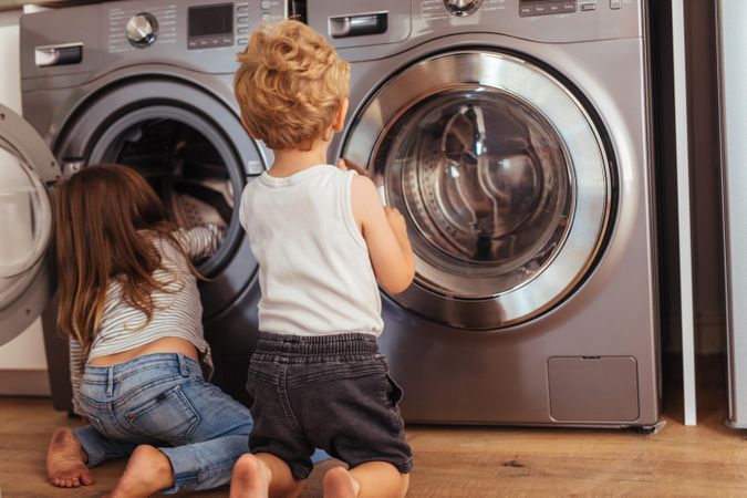 Rear view of children sitting near washing machine and playing
