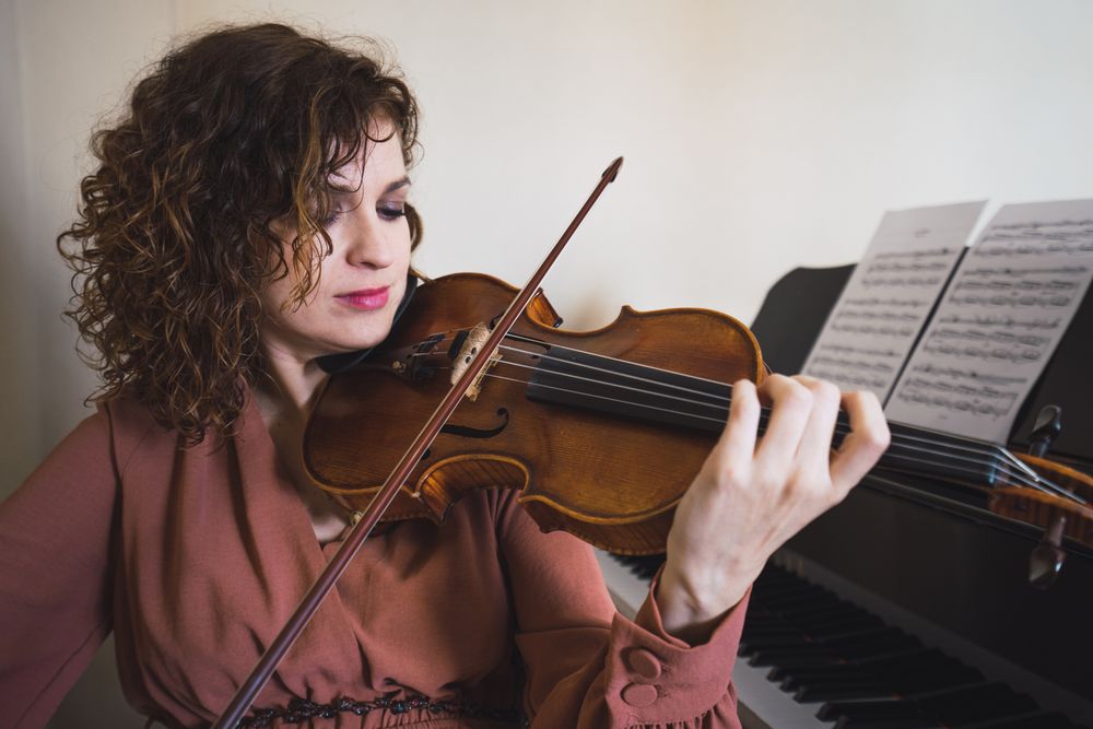 Pregnant woman playing on violin near piano in room